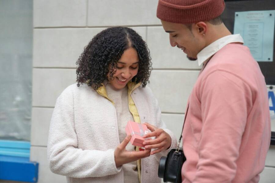 A couple joyfully exchanging a gift on a city street, symbolizing love and happiness