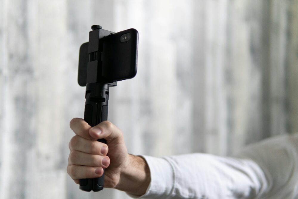 Close-up of a person holding a smartphone attached to a tripod for stability.