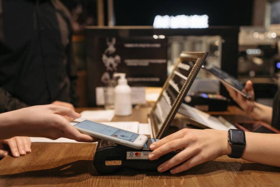 Hands using mobile for contactless payment at café terminal