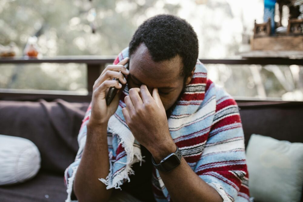 A man wrapped in a blanket looks distressed while talking on the phone outdoors