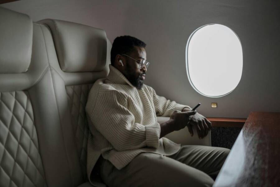 Bearded man in cozy sweater using smartphone on airplane, enjoying in-flight entertainment.