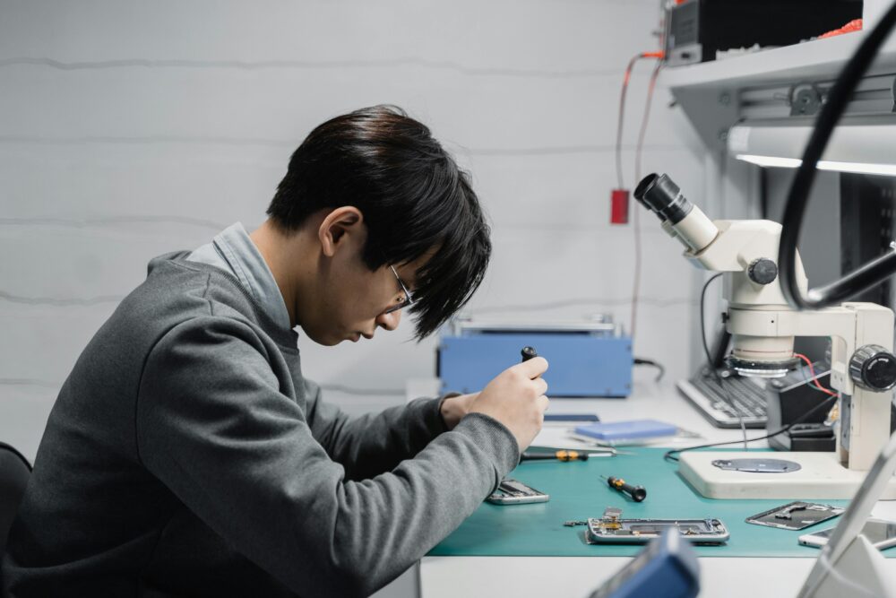 Professional technician repairing mobile devices using a microscope in a lab.