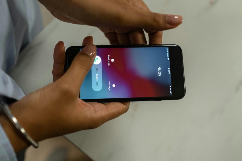 Close-up image of hands holding a smartphone receiving a call from Ruby on a marble surface.
