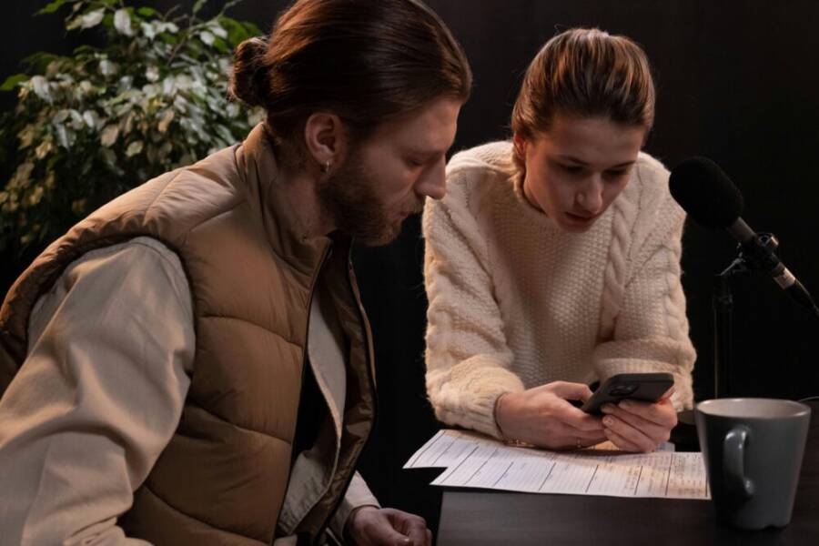 Two young adults engaged in podcast production, using a smartphone and microphone.