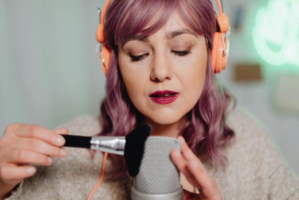 Close-up of a woman using a brush and microphone for ASMR in a cozy indoor setting.