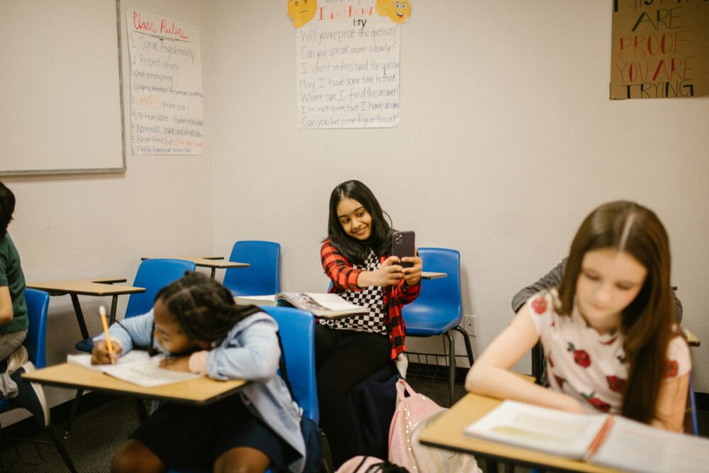 A diverse group of students in a classroom setting, one using a smartphone
