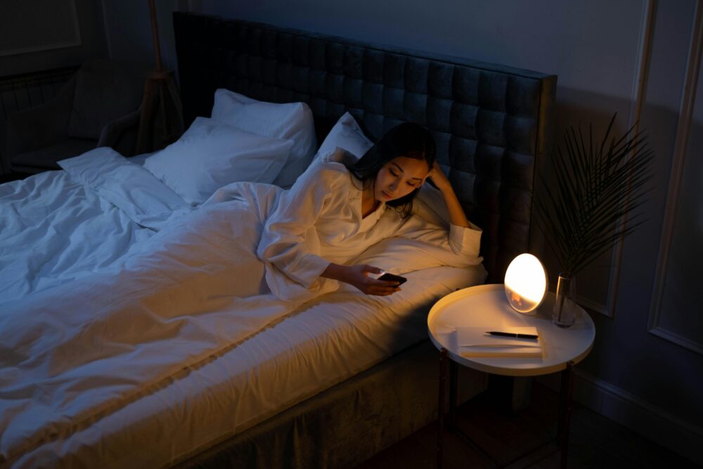 An Asian woman on a bed using her phone in a dim bedroom, reflecting on insomnia or night routines