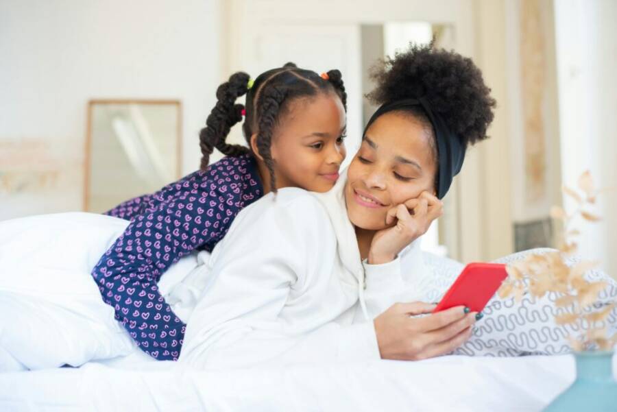 A heartwarming moment between a mother and daughter embracing while using a smartphone indoors