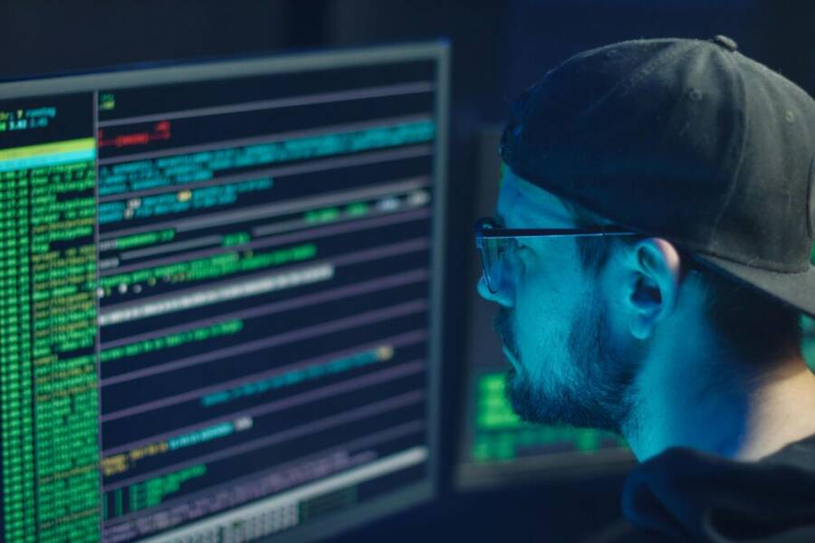 A cybersecurity expert inspecting lines of code on multiple monitors in a dimly lit office