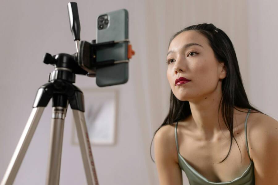 Asian woman recording a vlog indoors using a smartphone on a tripod