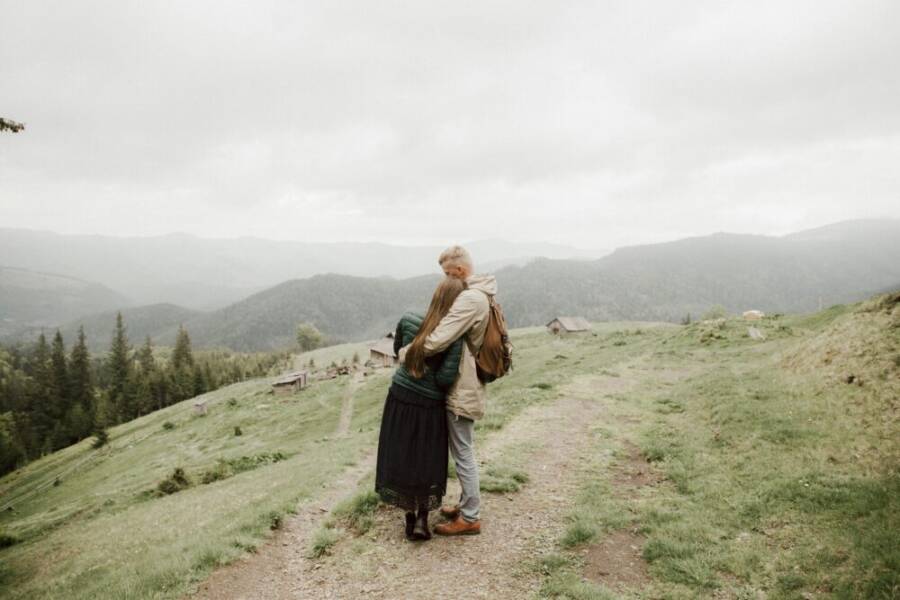 A couple exploring a misty pine forest with rolling hills