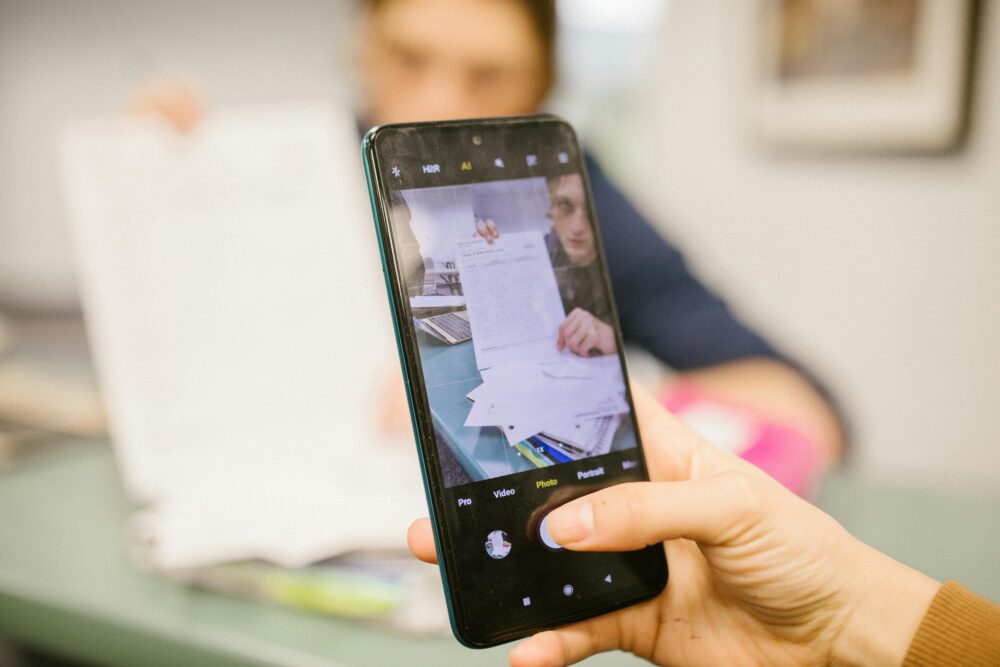 Close-up of student using smartphone to photograph examination papers in a classroom setting