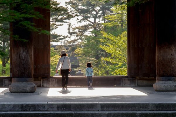 A family strolling through a temple gate surrounded by lush greenery in Kyoto, Japan