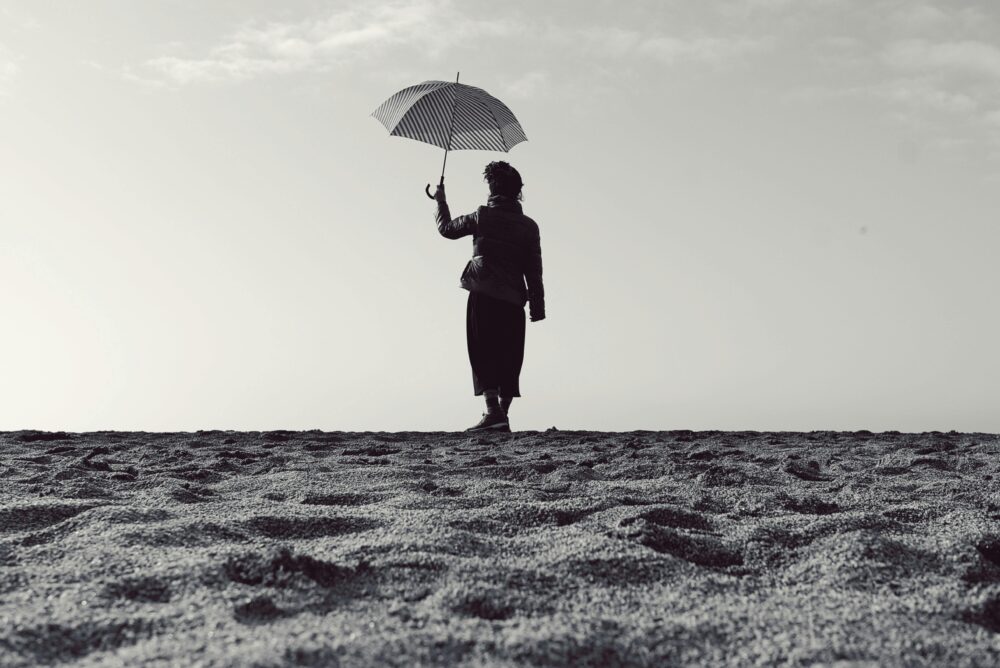 Black and white silhouette of a woman holding an umbrella while standing on a serene beach.