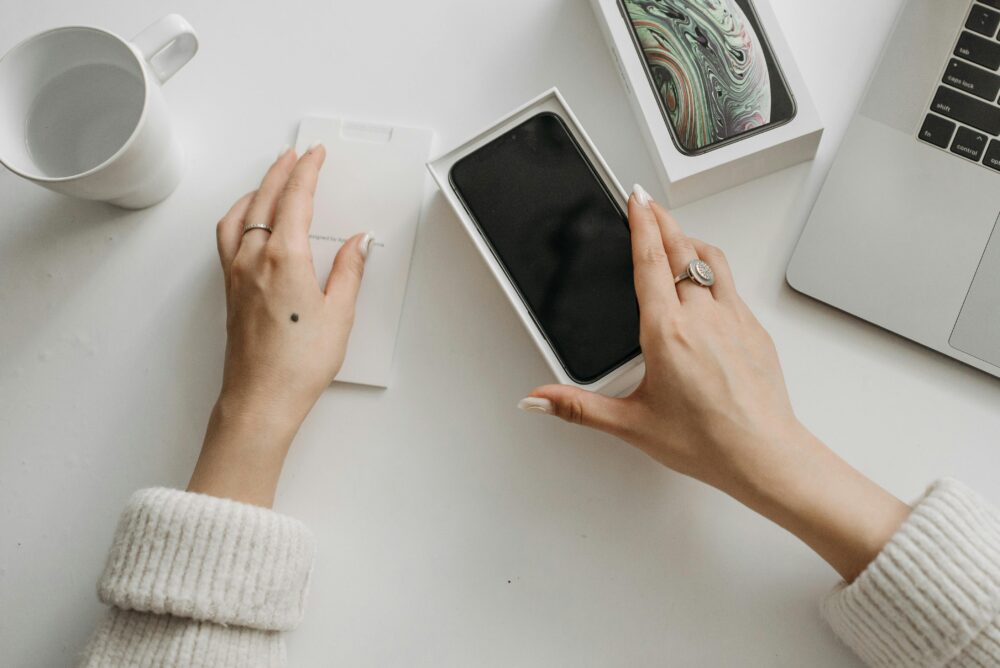 Woman unboxing a smartphone on a white table, showcasing technology and lifestyle