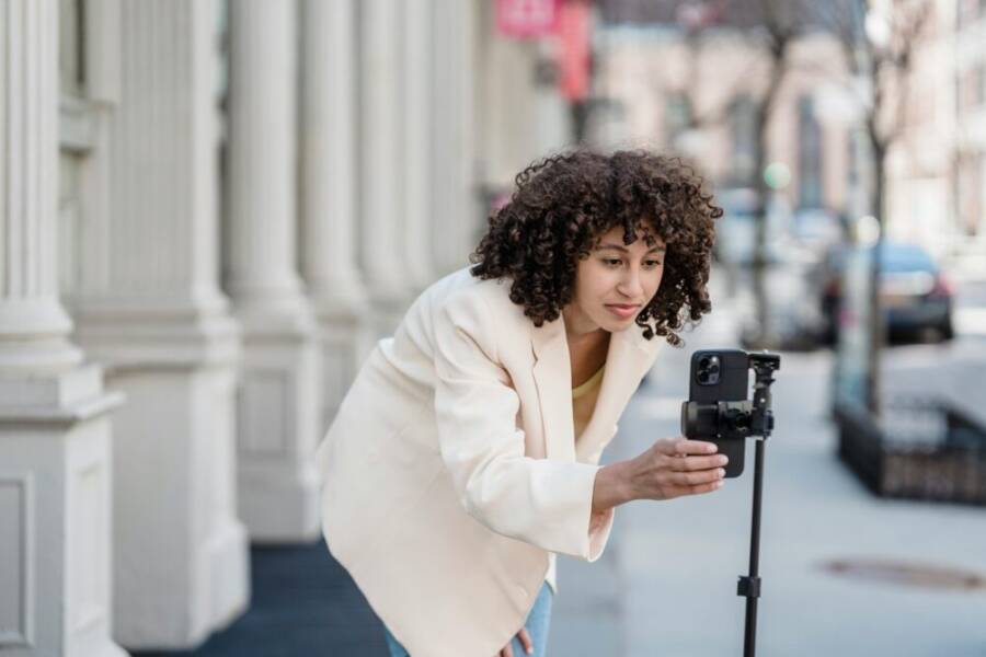 A young woman sets up her smartphone on a tripod in an urban setting, ready to record.