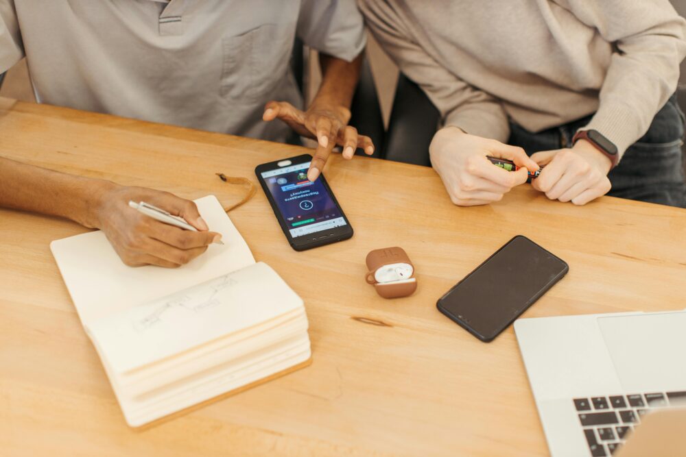 Teamwork at a table using smartphones, notebooks, and laptops to collaborate in an office setting.