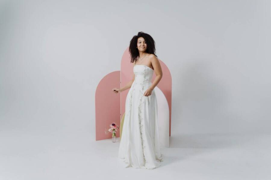 A beautiful bride in a white wedding dress smiling against a pink background, radiating elegance