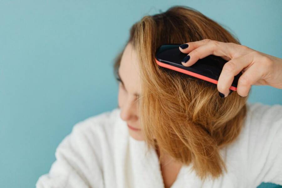 Close-up of a woman brushing her hair in a bathrobe, representing a daily grooming routine.