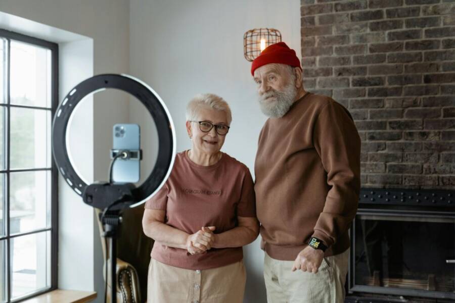 A charming elderly couple recording content indoors with a smartphone and ring light.