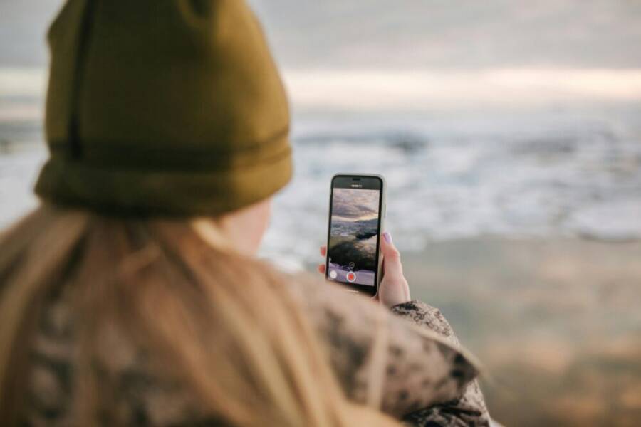 A person with a beanie using a smartphone to film the ocean view