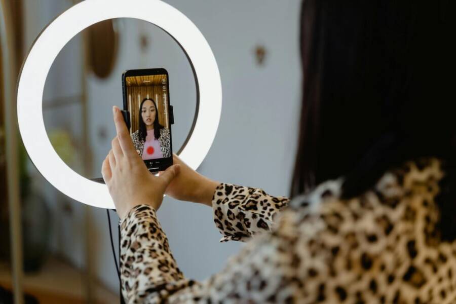 An Asian woman uses a smartphone and ring light for content creation