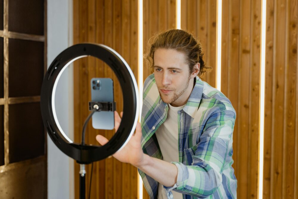 A young man sets up a smartphone and ring light for social media video recording, focusing on optimal lighting