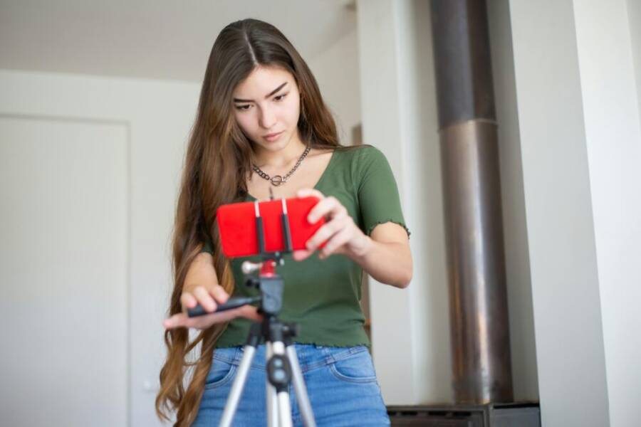 Young woman adjusting smartphone on tripod indoors, focusing on content creation.