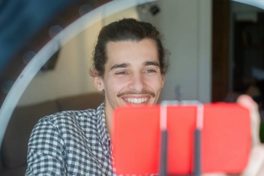 Happy man taking selfie for vlogging using smartphone and ring light setup indoors