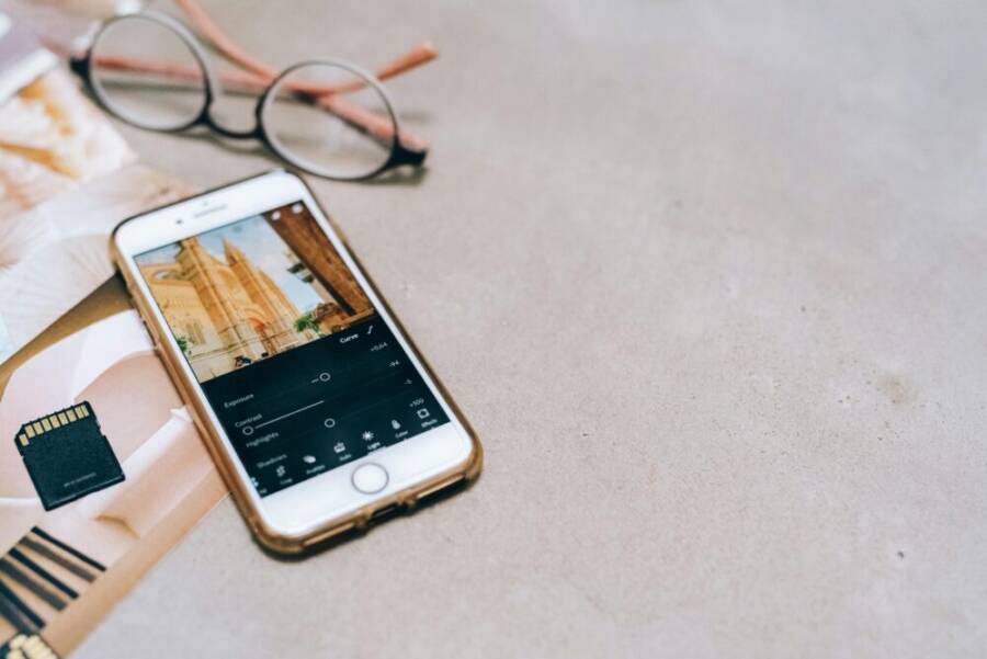 Smartphone displaying a photo editing app, next to a memory card and glasses on a table.