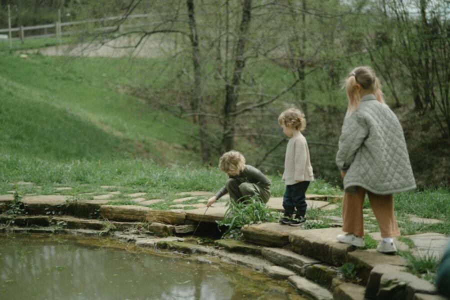 Three children exploring a pond in a lush, green setting during spring. A serene outdoor adventure.