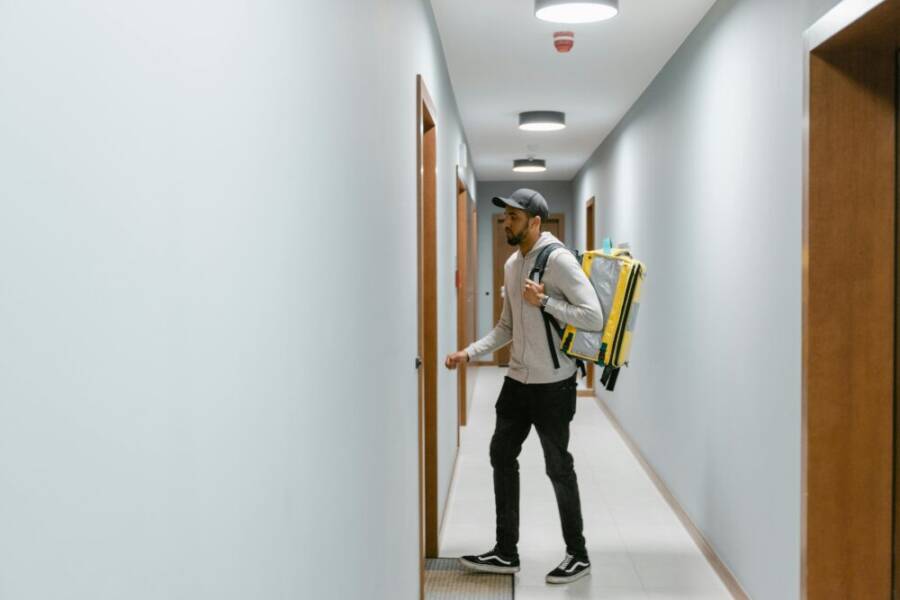 Courier with backpack entering an apartment hallway for delivery service