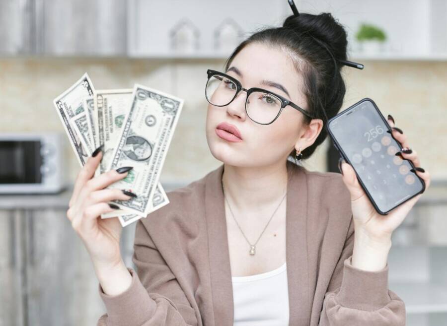 Woman holding cash and smartphone displaying calculator, highlighting personal finance management