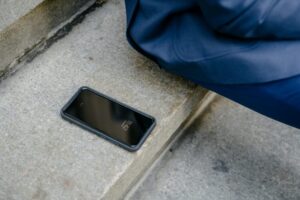 A smartphone is left unattended on concrete steps outdoors, next to a person in blue clothing