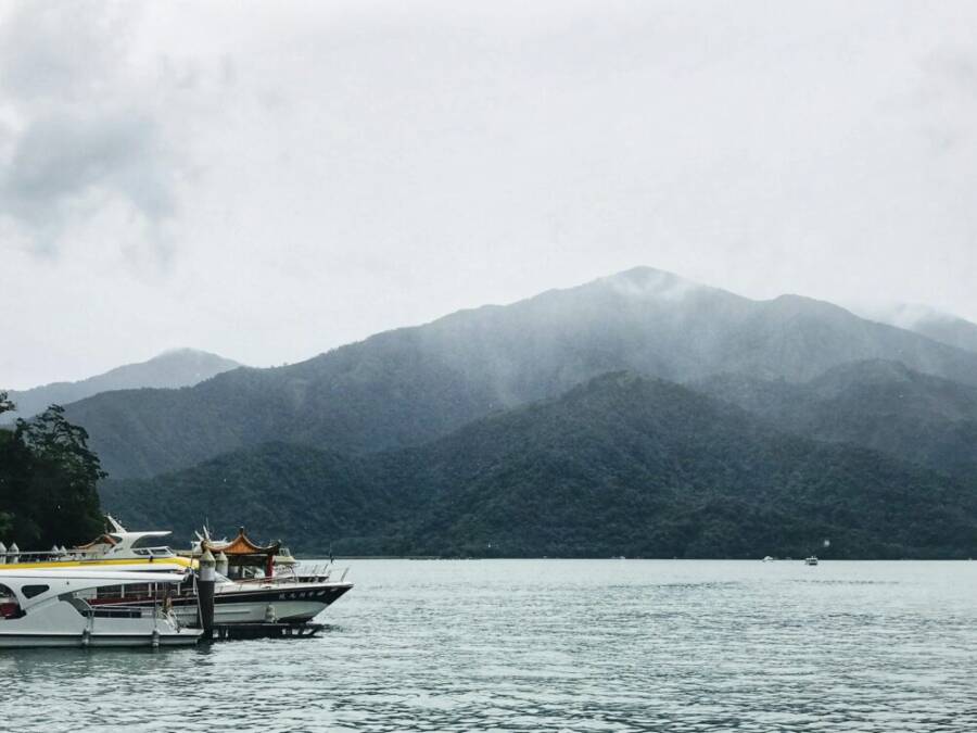 A tranquil scene of boats docked at Sun Moon Lake, surrounded by misty mountains in Taiwan.