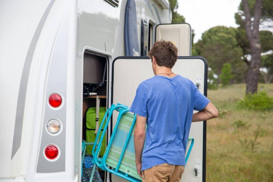 A man loads camping gear into an RV, preparing for an outdoor adventure in a lush, green environment