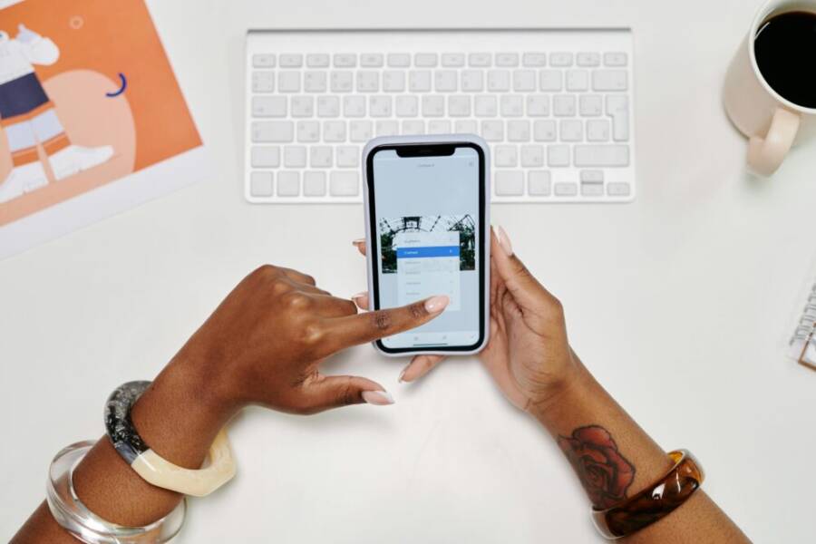 Close-up of hands using a smartphone at a desk with a keyboard and coffee cup