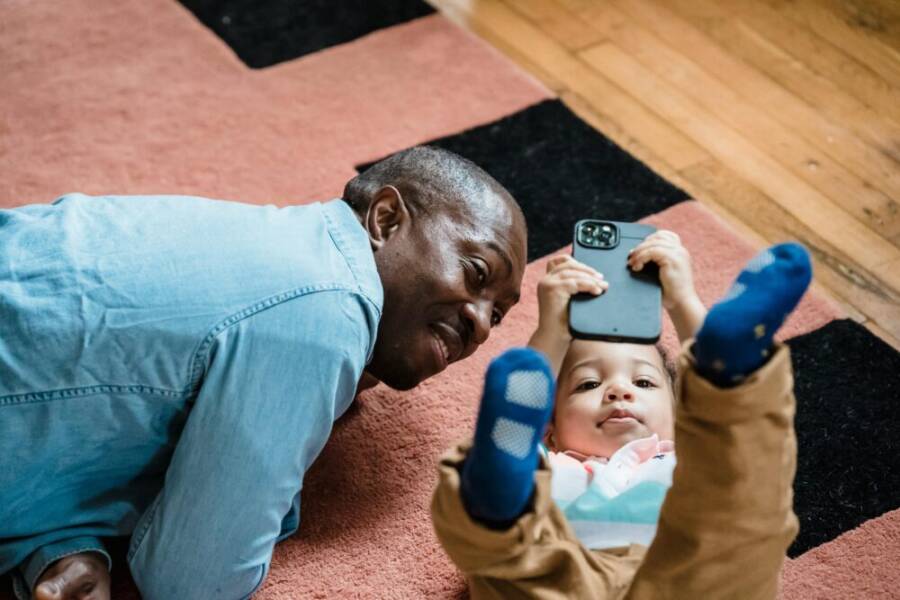 A father and child using a smartphone together on a cozy rug