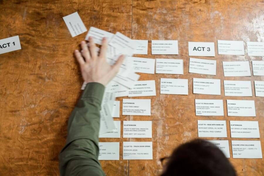 A person arranging storyboard cards on a wooden table for a film script planning session