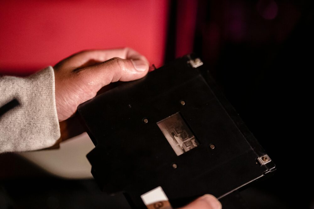 Close-up of hands holding a film negative holder in a dimly lit darkroom setting.