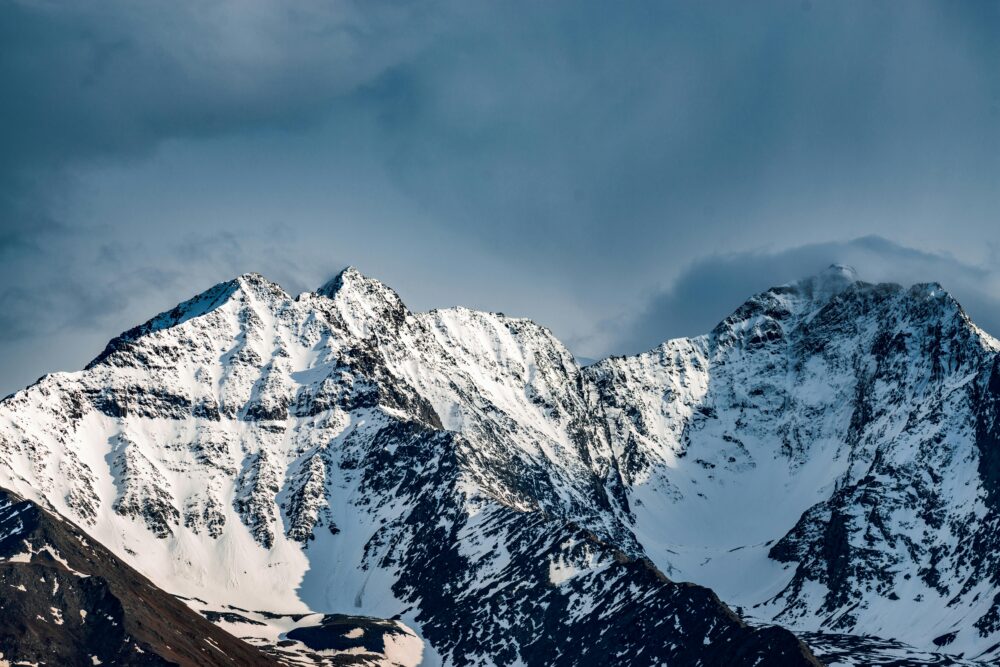 A stunning view of snow-covered mountain peaks with a dramatic cloudy sky backdrop.
