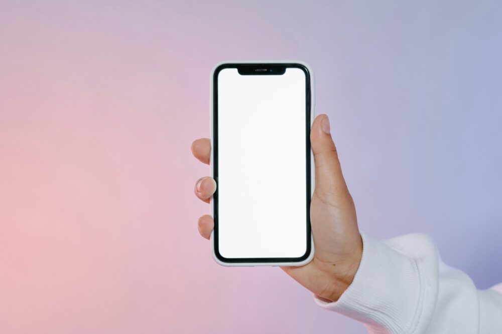 Close-up of a hand holding a smartphone with a blank screen against a colorful gradient backdrop.