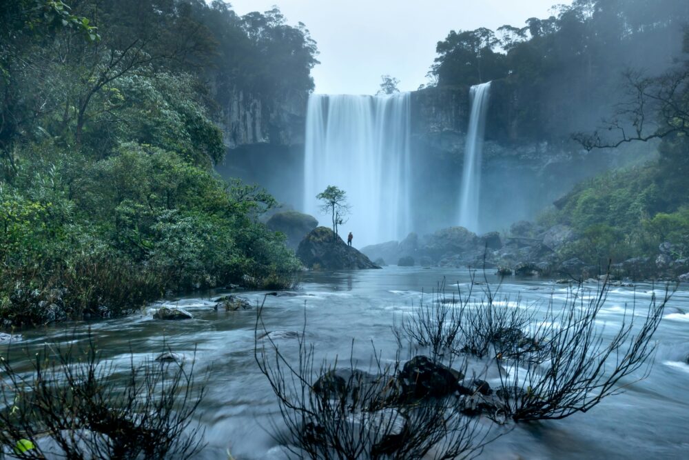 A lone figure by a misty forest waterfall