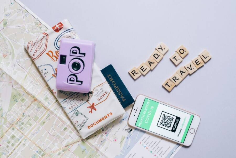 Travel essentials including a map, passport, camera, and smartphone with COVID-19 health passport for modern travel preparations