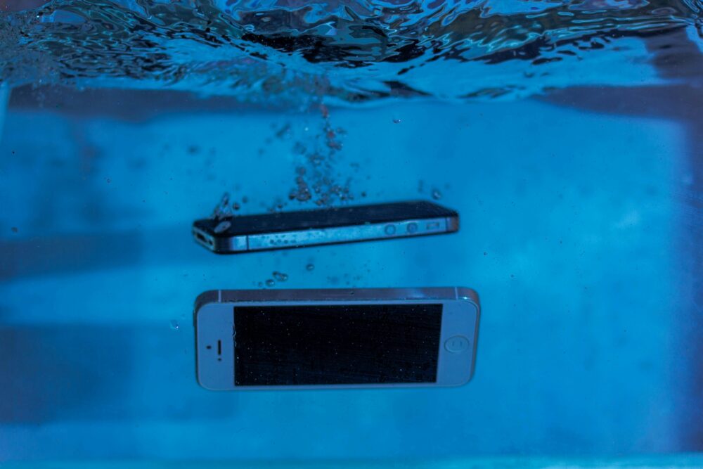 Two smartphones immersed underwater with bubbles, showcasing water-resistant test perspectives.