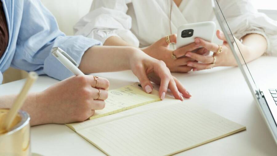 Women collaborating in a workspace with a notebook and smartphone, focusing on productivity.