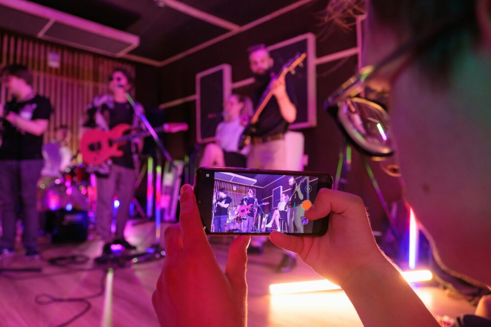 A dynamic band performs live in a music studio, captured on a smartphone.