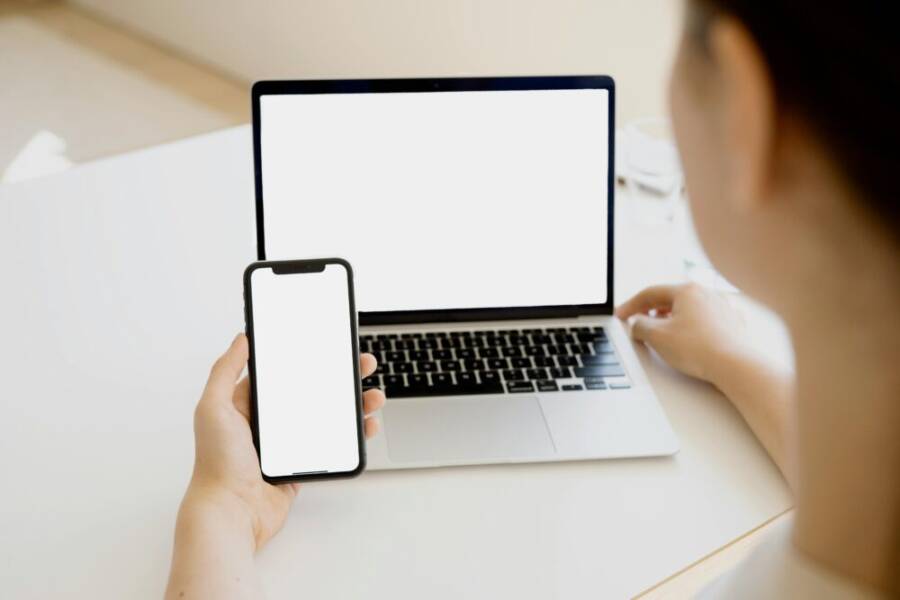 A woman holding a smartphone in front of a laptop, creating a seamless tech environment