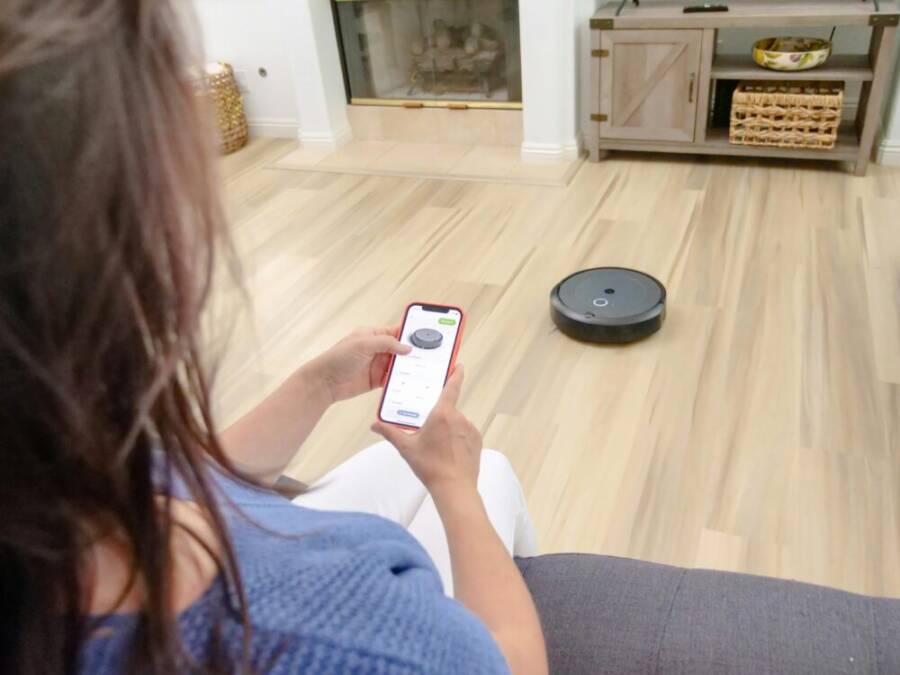Overhead view of a woman controlling a robot vacuum using a smartphone app on a wooden floor
