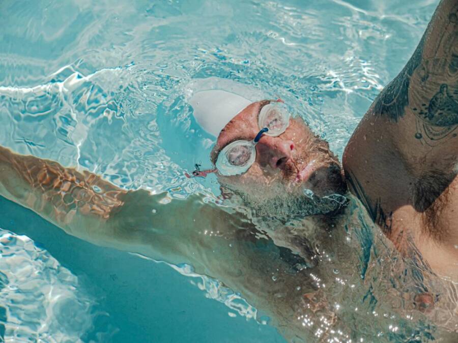 An adult male swimmer training in a pool, wearing goggles and a swim cap, captured underwater.